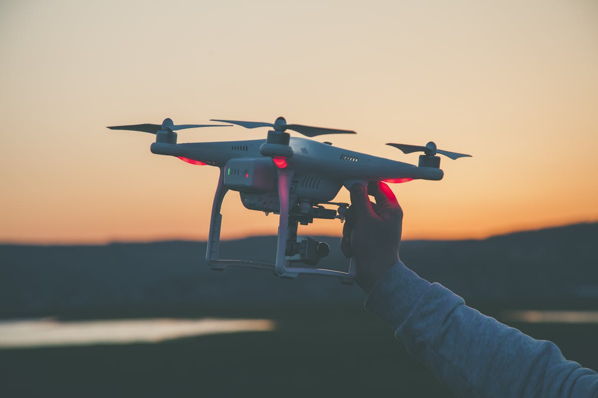 Silhouette of a drone and hand against a colorful sunset backdrop.